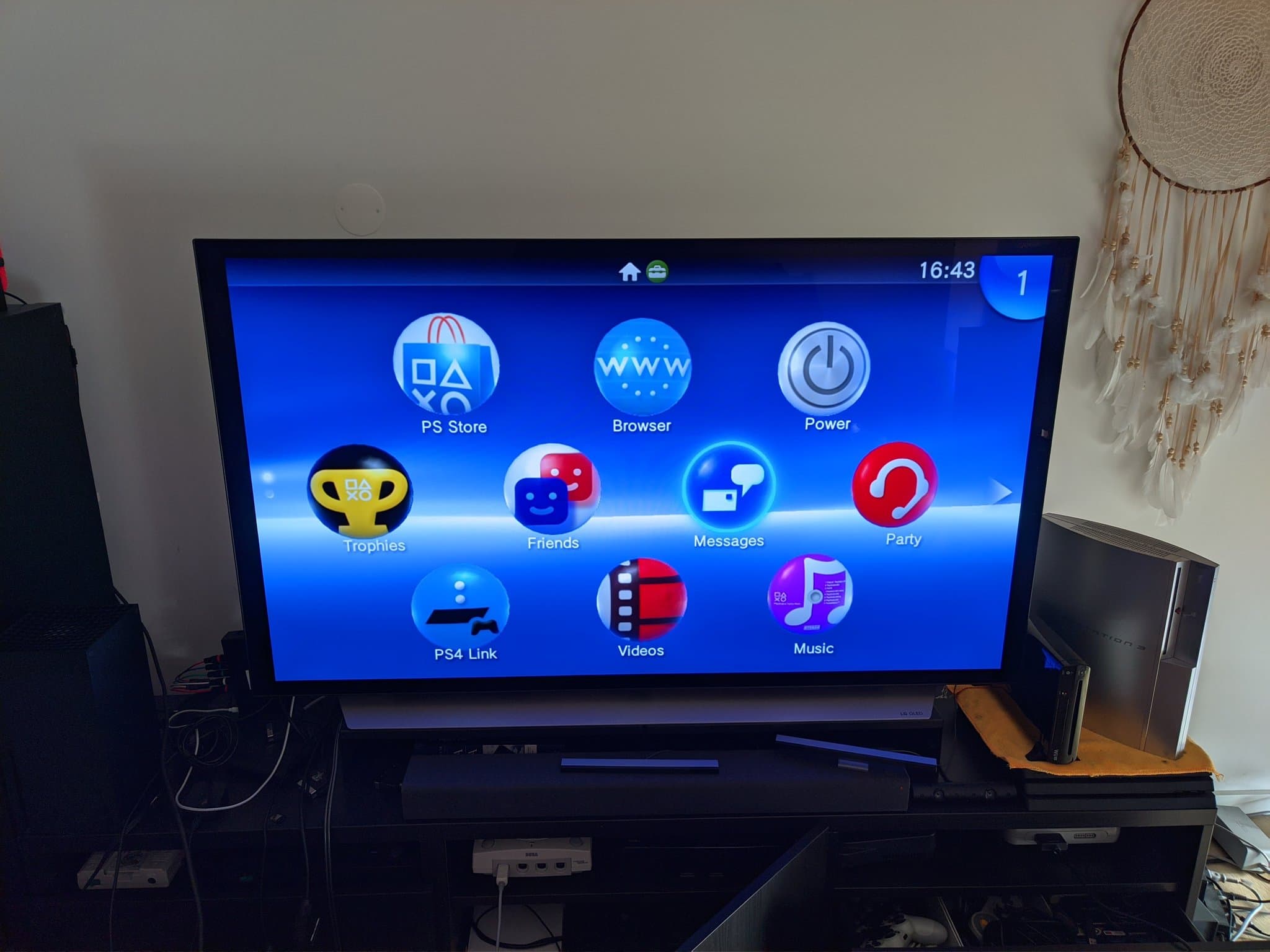 PS Vita TV home menu displayed on TV, showing restored unit with custom firmware installed, positioned on black stand in living room setup.