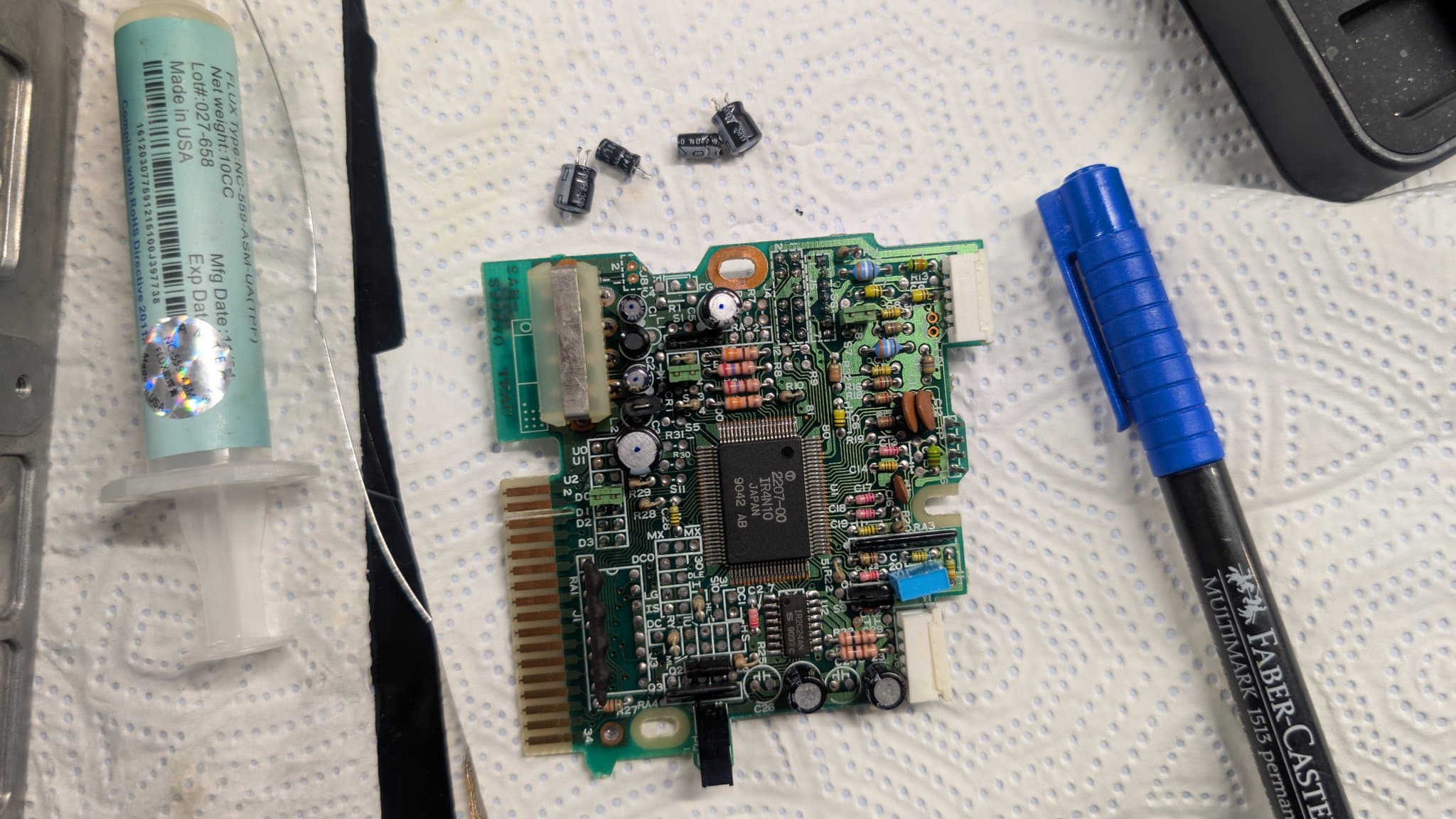 A floppy drive PCB from the Sharp X68000 Pro II just after recapping, with a flux syringe and a felt-tip pen (used to mark each newly replaced capacitor with a dot) alongside.