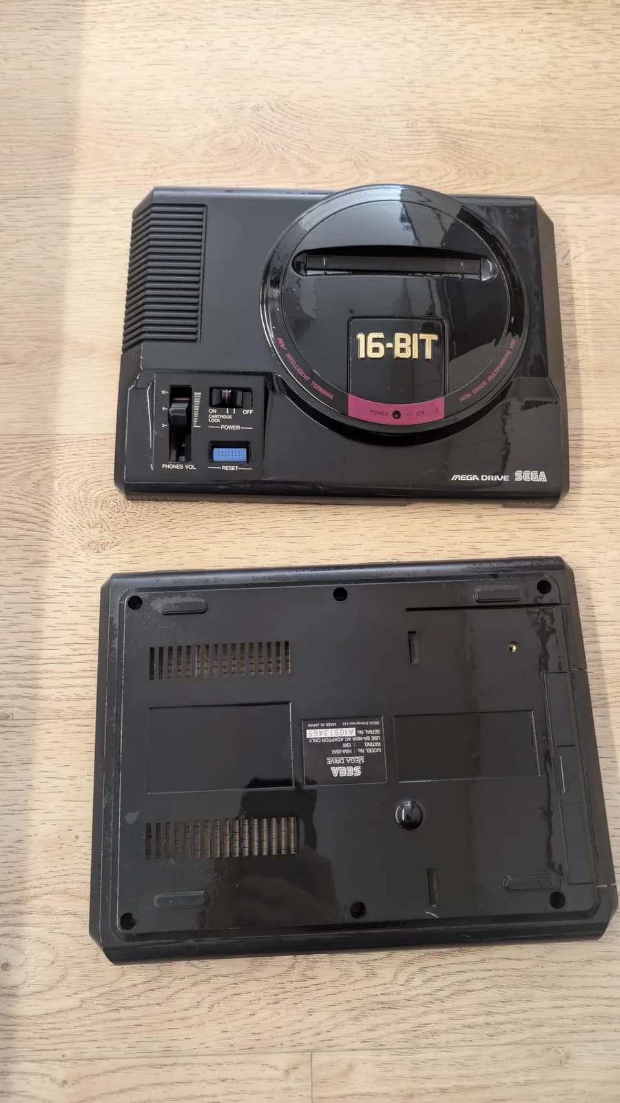 Sega Mega Drive 16-Bit top and bottom shells displayed separately on wooden surface, showing cleaned casing before reassembly.