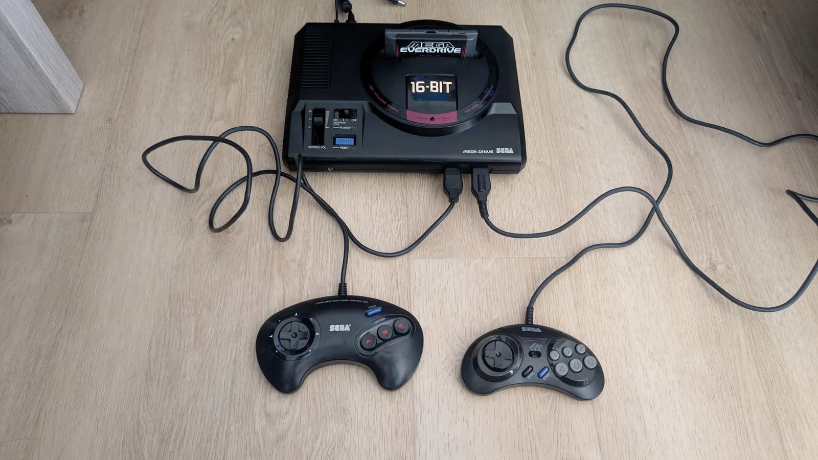 Sega Mega Drive 16-Bit console with two cleaned controllers and cables on wooden surface, ready for delivery.