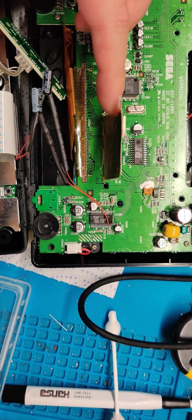 Nomad motherboard with soldering iron applying audio mod components; 10uF capacitors and 10k resistors visible on circuit board for Master System/Mega-CD audio restoration.