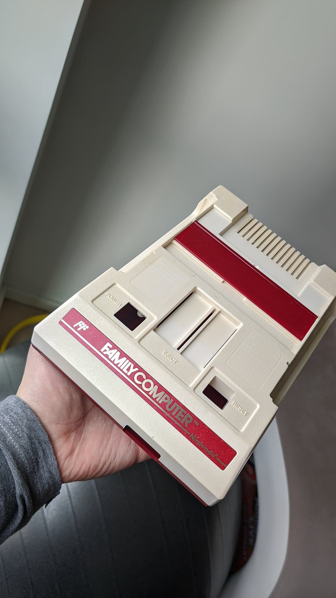 Famicom top shell after retrobrighting, the cream and red casing with its fresh FAMICOM front decal, held up to the light.