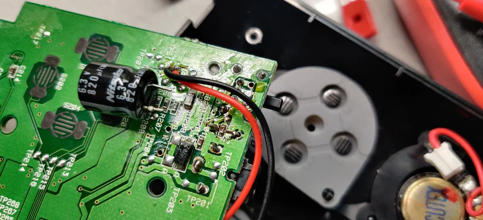 Sega Nomad PCB closeup showing poor solder joint on capacitor leg near red wire; capacitor leg wiggling freely in through hole with inadequate solder connection.