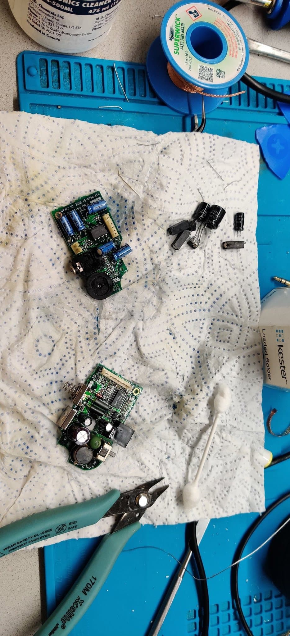 A Game Gear sound board and power board after recapping, the removed old electrolytic capacitors scattered around them on the work mat.
