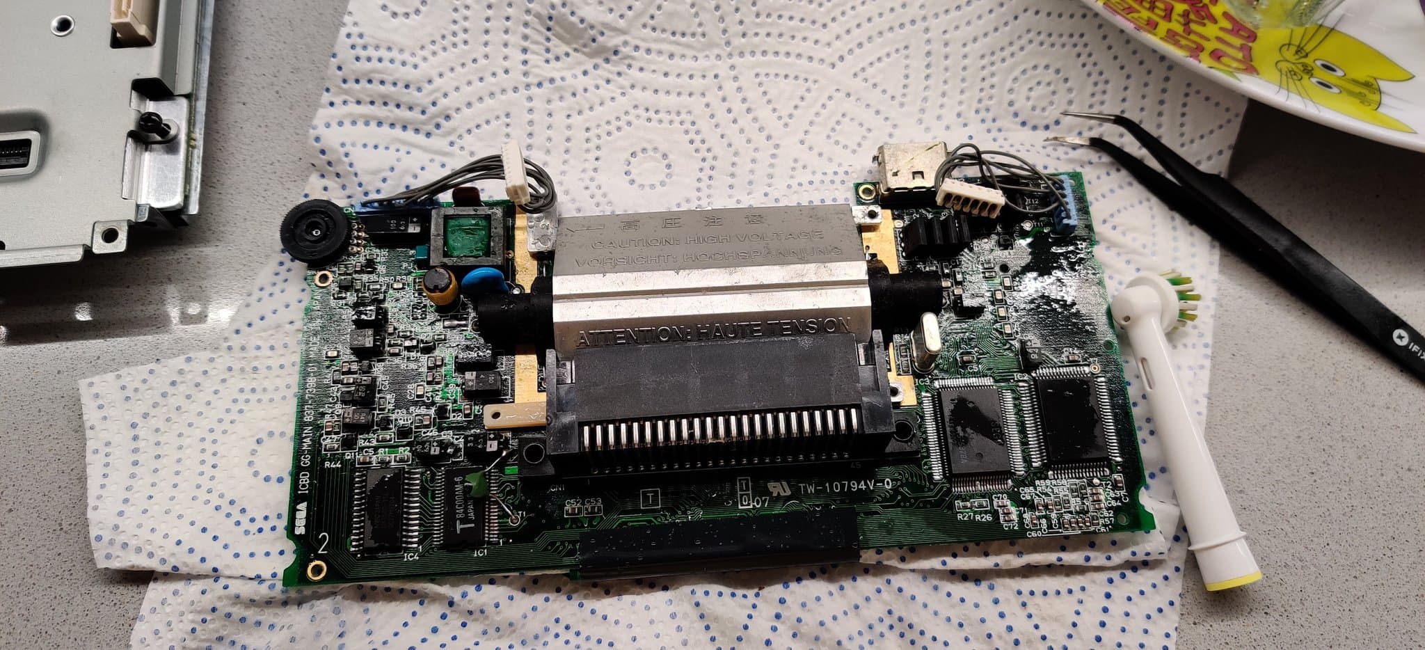 One of the Game Gear boards being scrubbed with white vinegar and a toothbrush to neutralize the alkaline capacitor electrolyte, contamination still visible on the board.