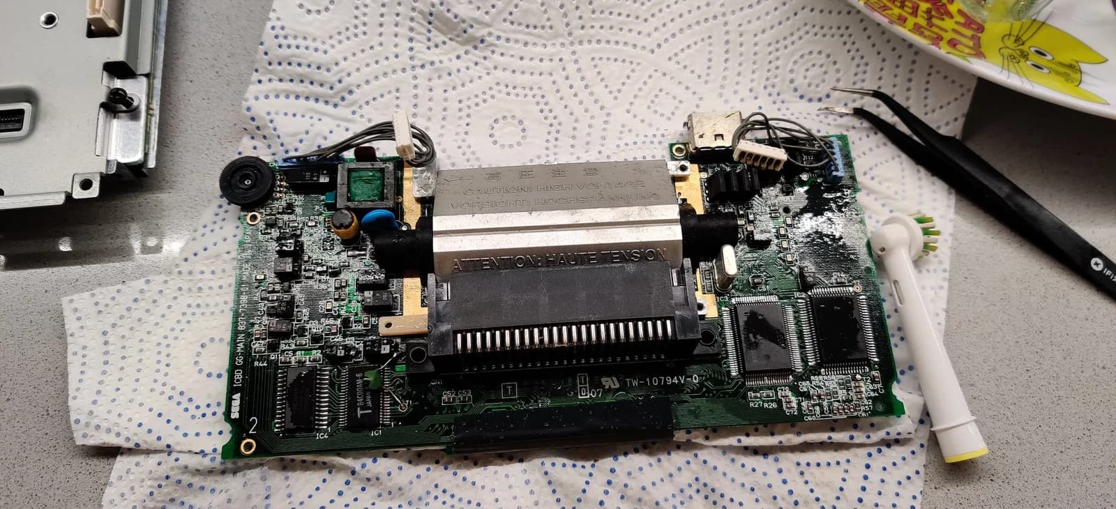 One of the Game Gear boards being scrubbed with white vinegar and a toothbrush to neutralize the alkaline capacitor electrolyte, contamination still visible on the board.