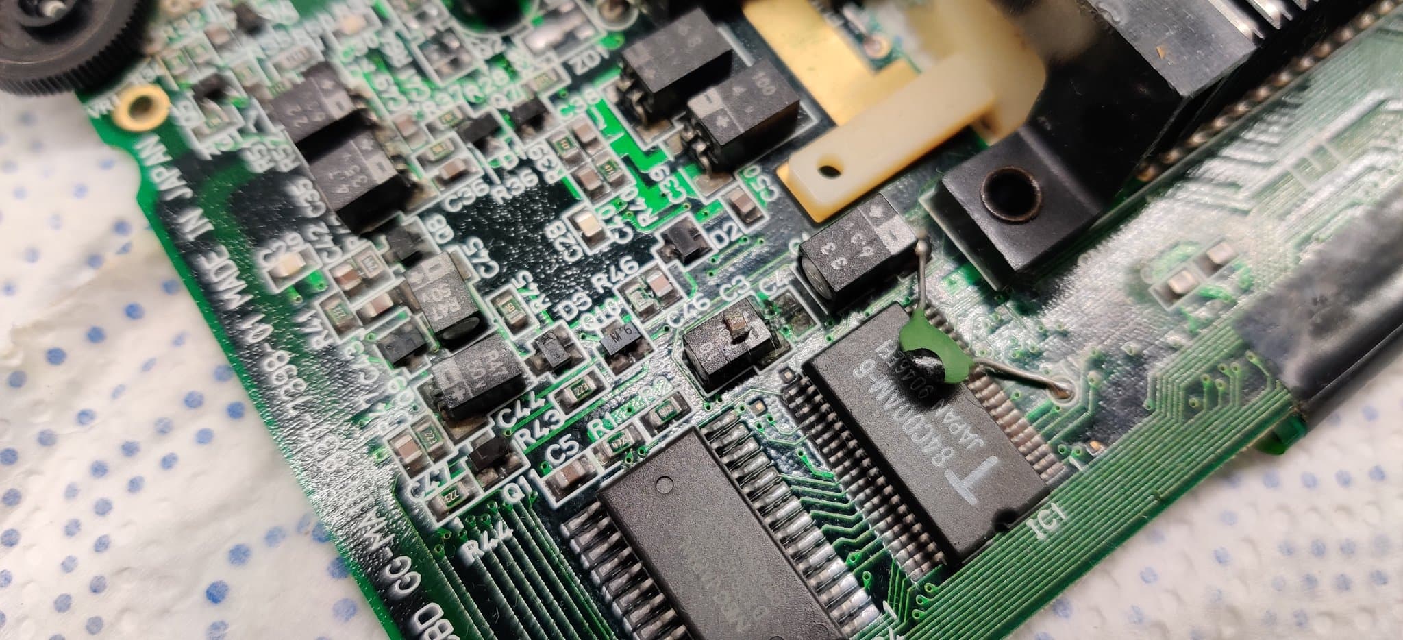 Close-up of a Game Gear board with heavy electrolyte contamination and corrosion on the capacitor pads and nearby components, nothing detached or loose.