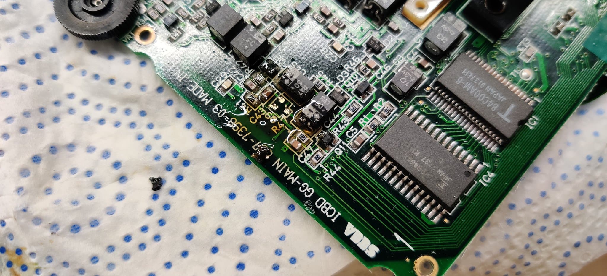 A cleaned-up area of a Game Gear board where flux was used to lift electrolyte contamination from the SMD solder joints, the transistor Q9 missing from its footprint after the contamination there loosened it during cleaning.