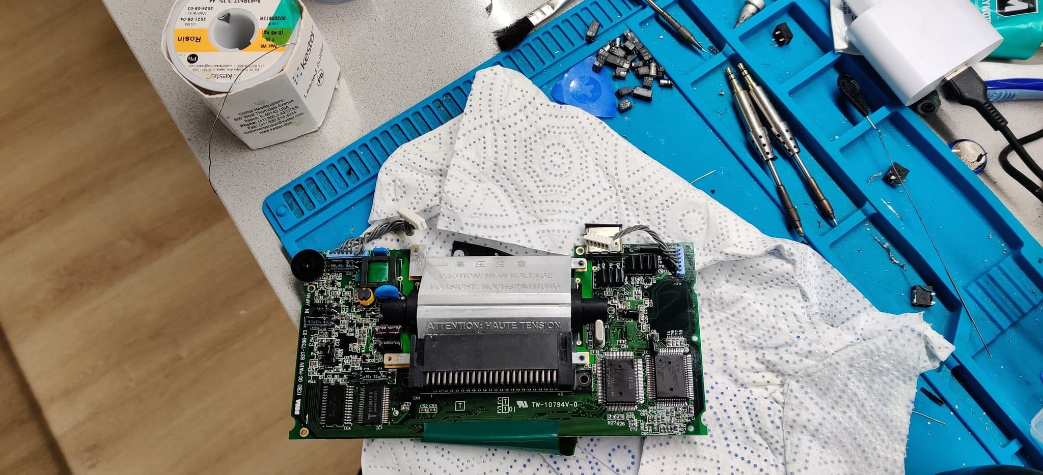 A single Game Gear board after recapping, all of its ICs reflowed to clear electrolyte contamination, with the pile of old capacitors visible at the top of the shot.