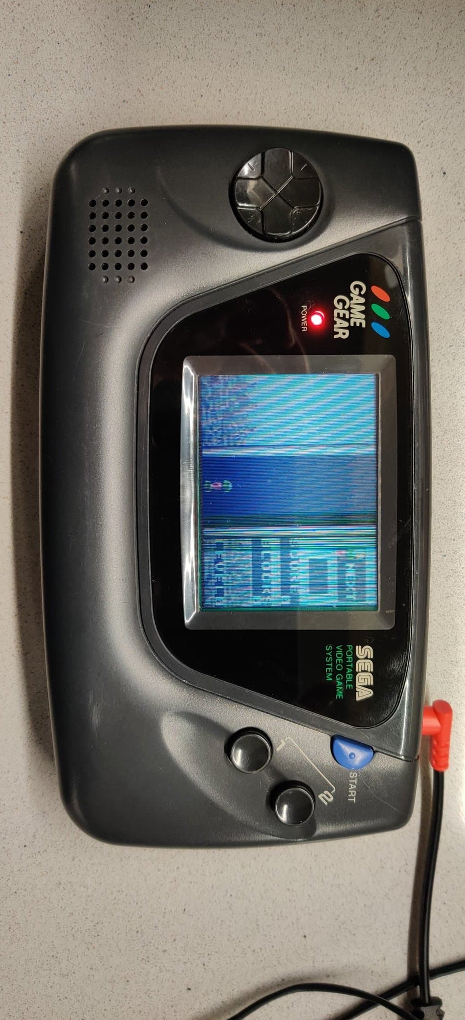 One of the two Sega Game Gears powered on after the work, its screen showing a picture broken up by defective horizontal lines, the partial-success unit.