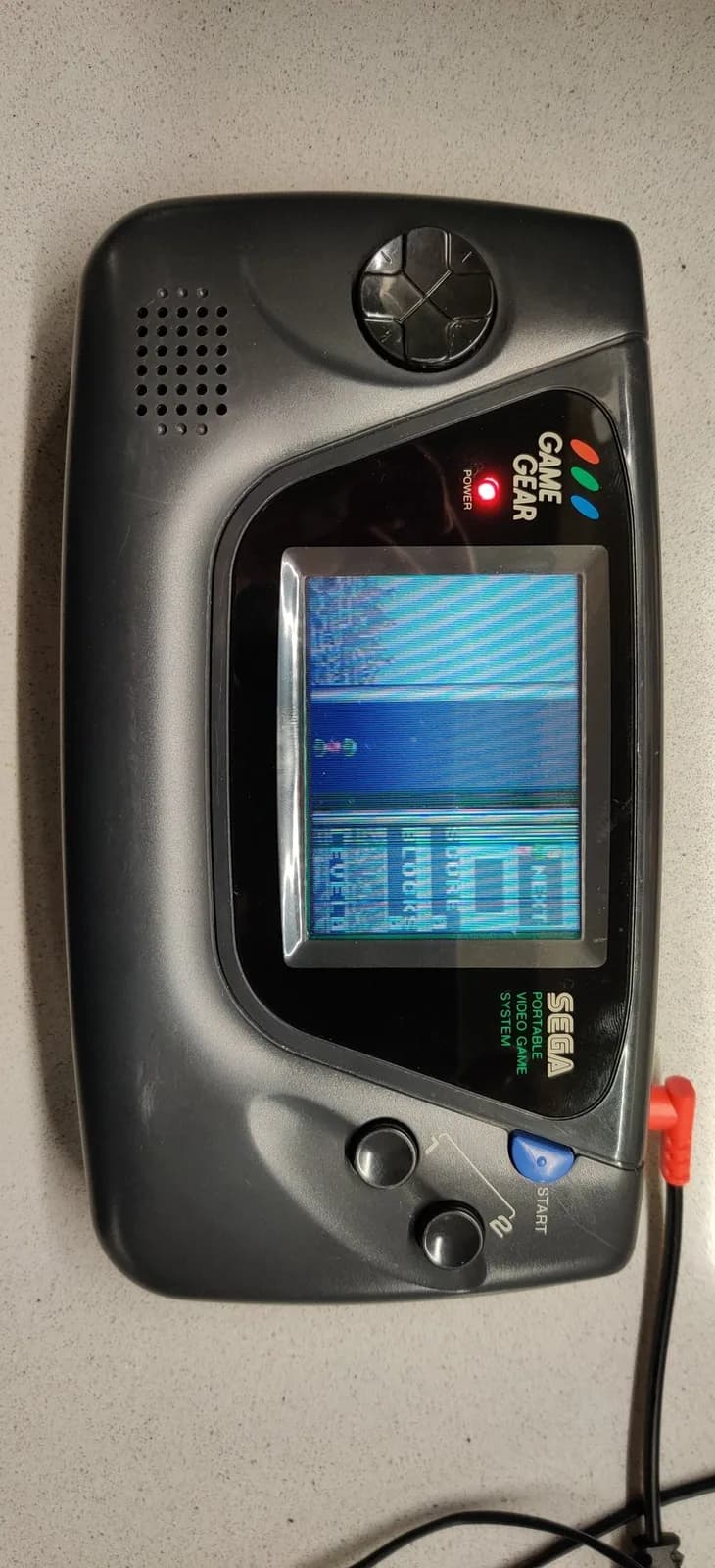 One of the two Sega Game Gears powered on after the work, the console turned on its side rather than its usual landscape orientation, its screen showing Columns broken up by defective vertical lines, the partial-success unit.
