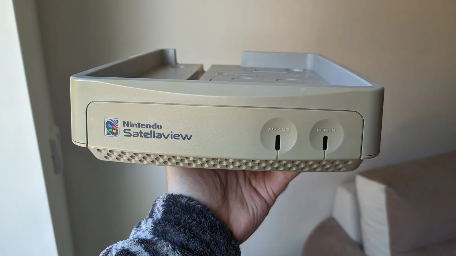 Nintendo SatellaView shell held in hand after retrobriting, showing cream-colored plastic with ACCESS and POWER buttons visible.