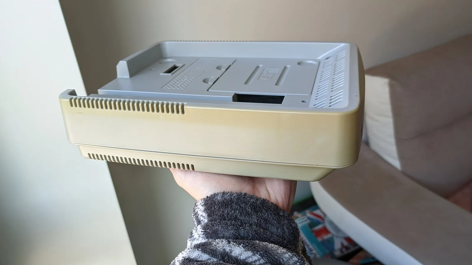 Hands holding a retrobrited Nintendo SatellaView unit showing the cream-colored plastic shell and grey top panel with ventilation grilles.