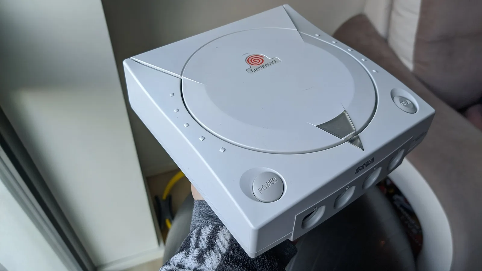 The Sega Dreamcast VA0 console after retrobriting, its white shell restored, held over a towel near a window, lid closed, showing the swirl logo, the POWER button and the front controller ports.