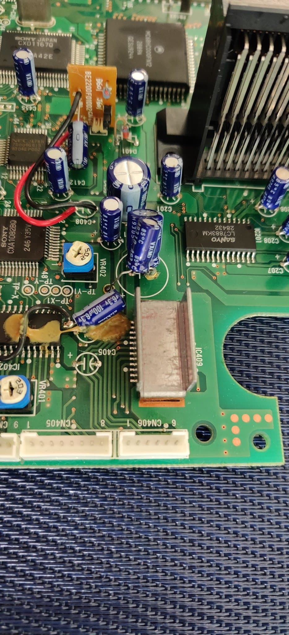 Sega Mega-CD 2 motherboard showing the factory bodge wires and electrolytic capacitors, the caps held down with factory glue or resin (not damaged), before the recap.