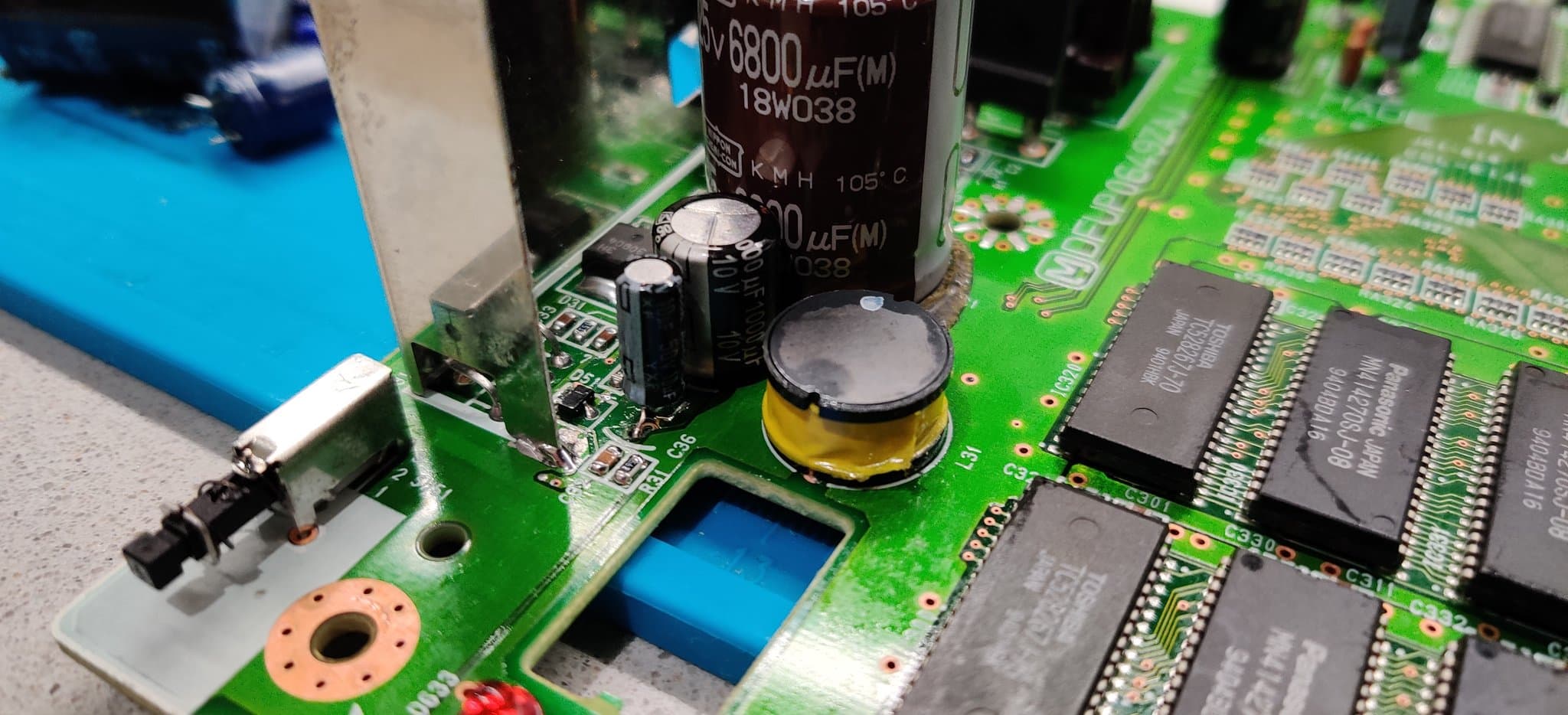 Panasonic FZ-1 PSU board mid-repair: large electrolytic caps, IC chips, bridged traces with solder, flux residue, and damaged through-holes from trace restoration work.
