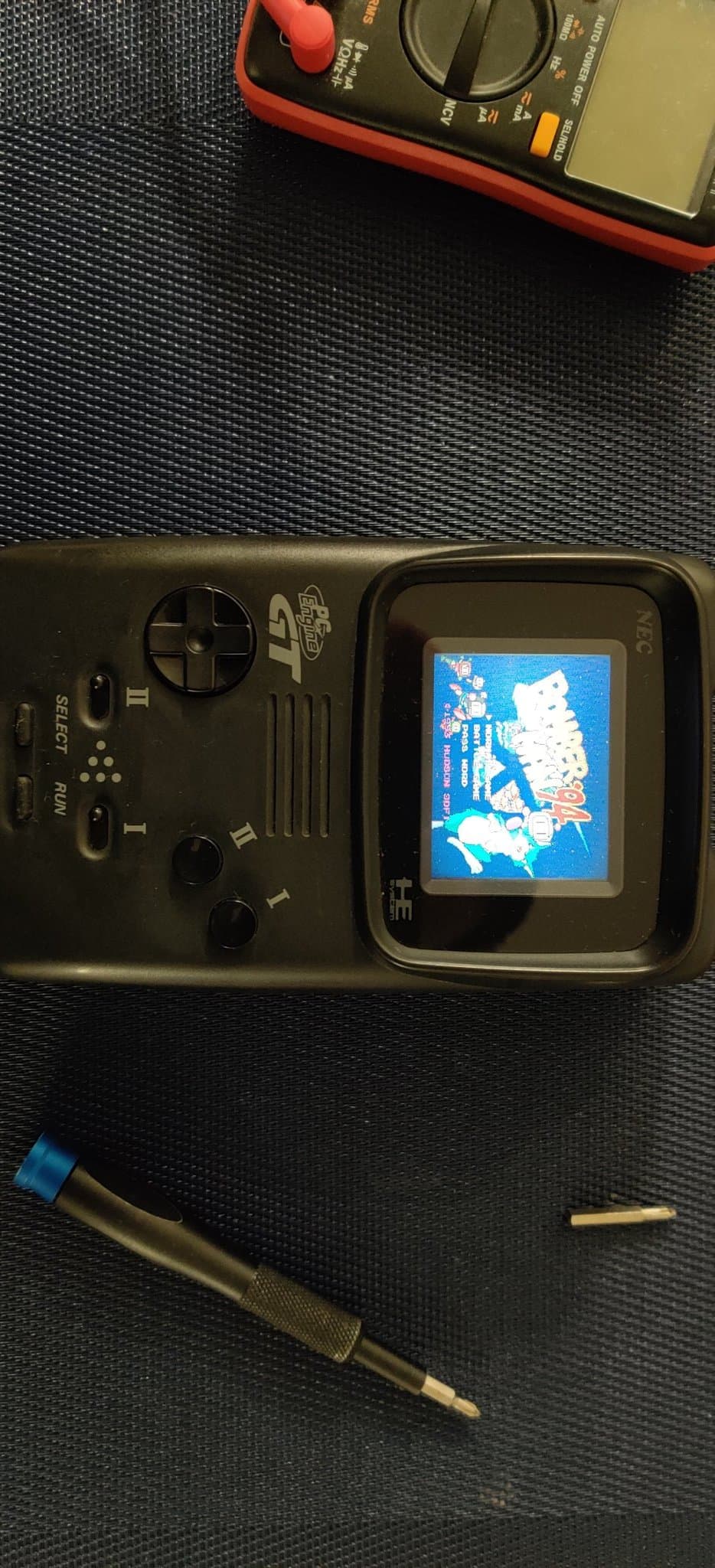PC Engine GT handheld powered on, its screen showing Bomberman '94 (run from a Turbo Everdrive v2) after the recap and jailbar fix, on the workbench.