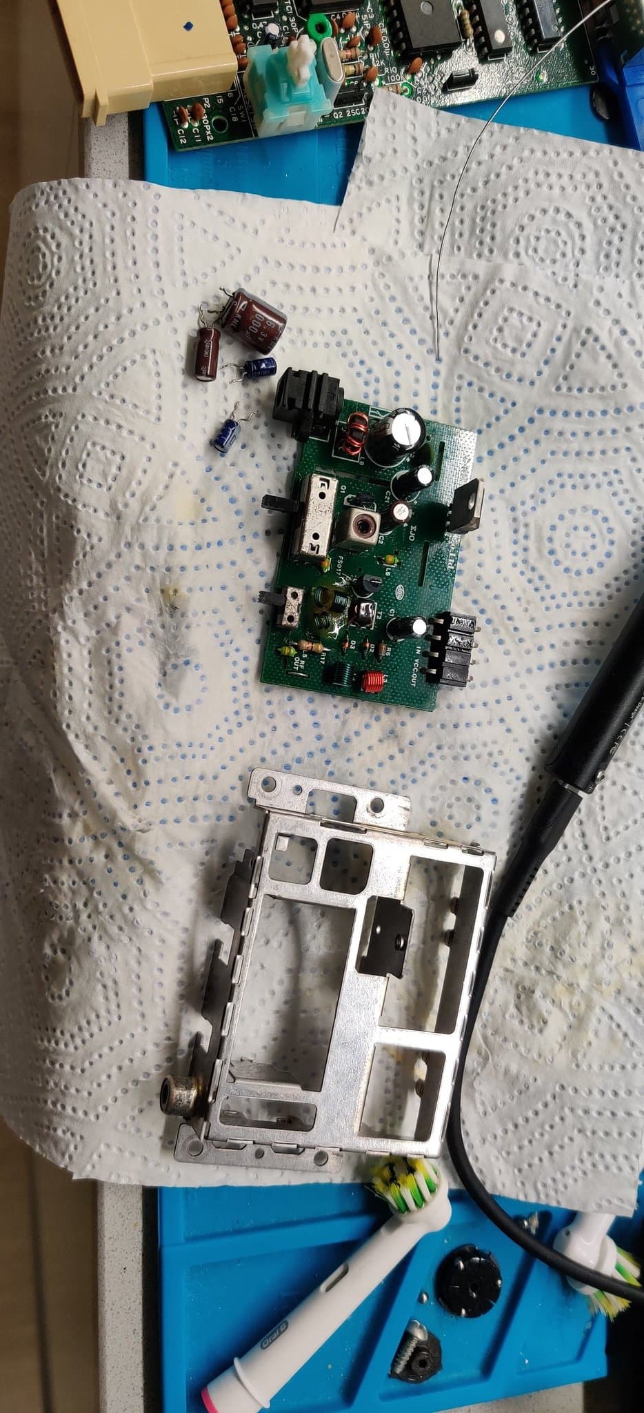 Famicom power board after recapping, with the new electrolytic capacitors installed and the old removed caps set beside it on the bench.