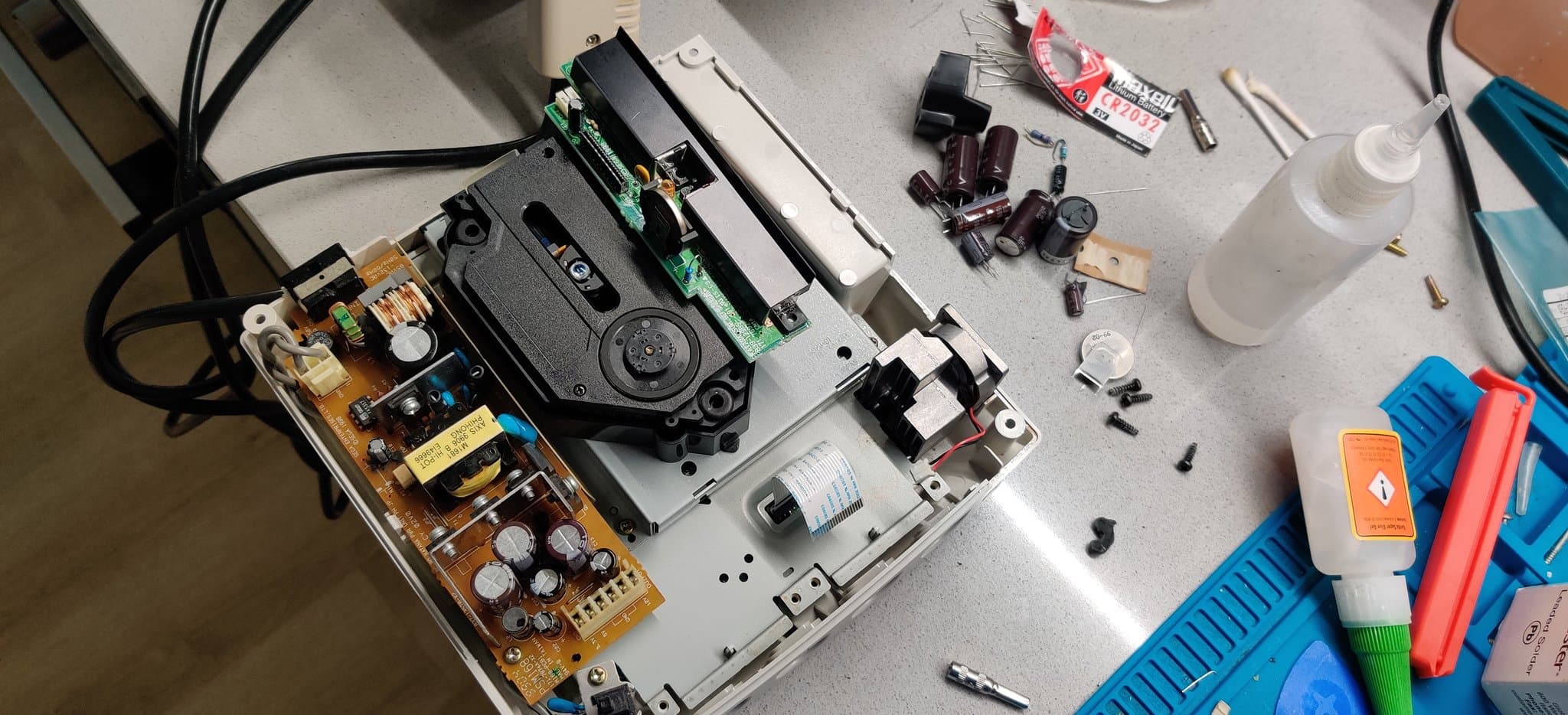 Dreamcast VA0 disassembled for refurbishment: PSU with capacitors, controller PCB, optical drive, GDEMU mod, and scattered components on work surface.