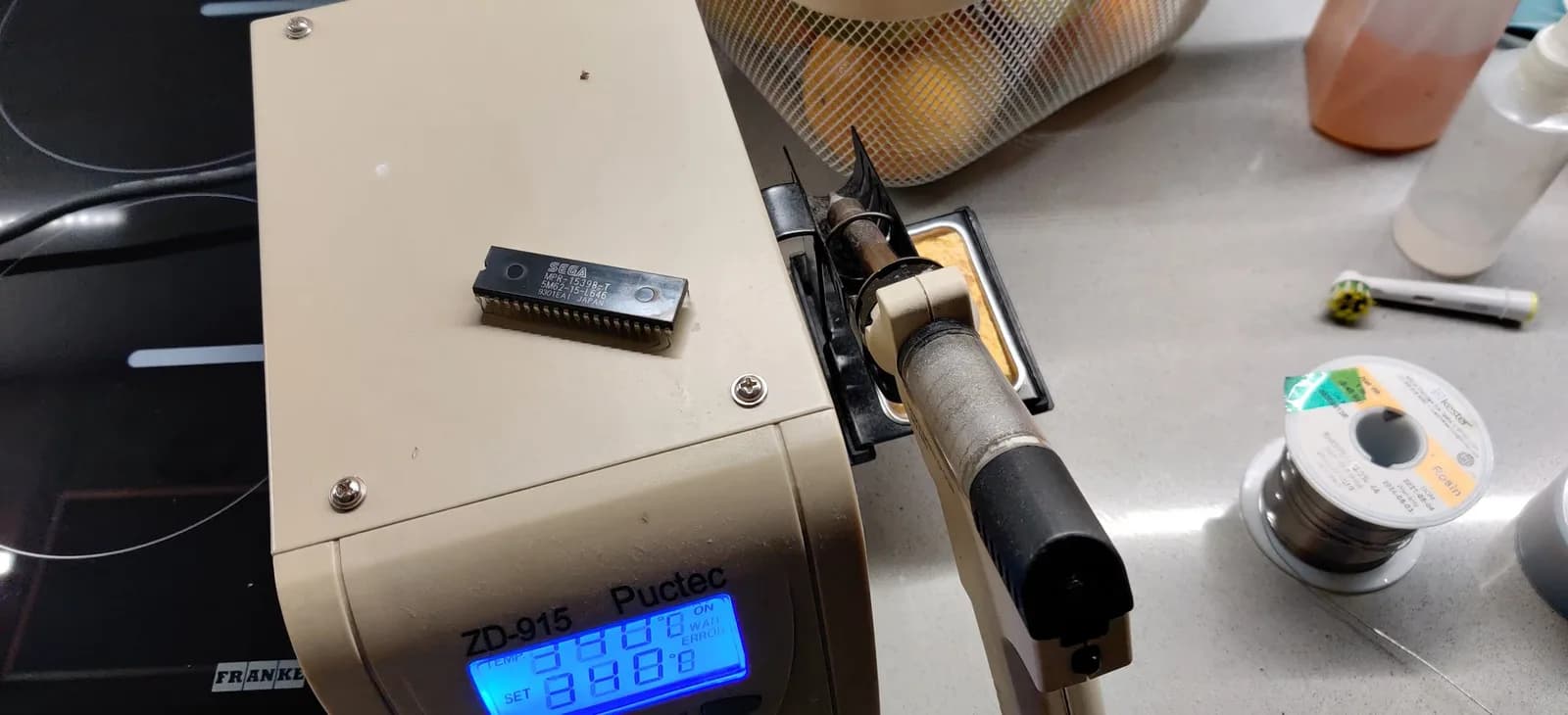 The original Sega Mega-CD 2 BIOS chip, freshly desoldered, resting on top of a ZD-915 Puctec desoldering station, with a soldering iron and solder spool nearby during the repair.