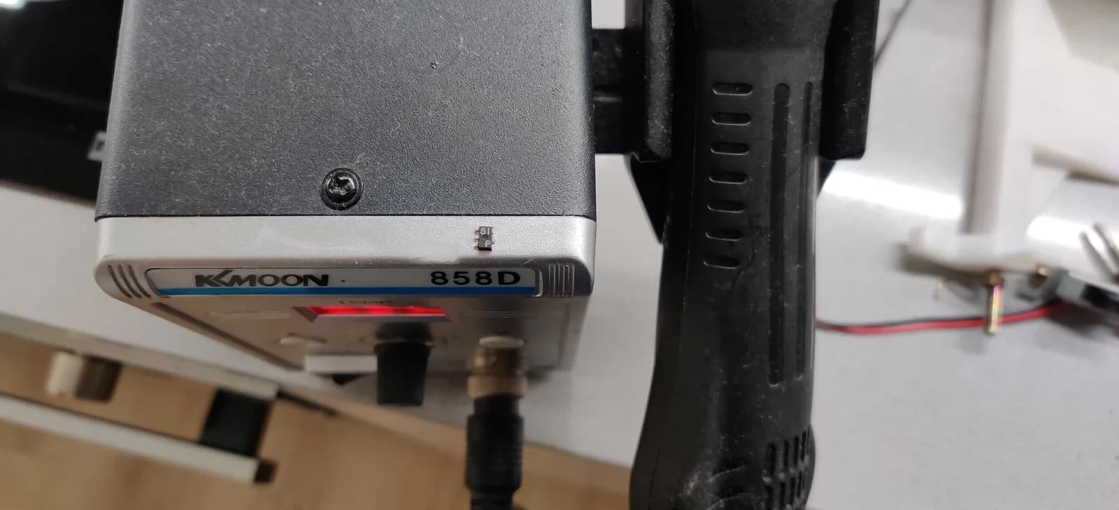 Close-up of a KKMOON 858D bench station on the workbench, its red temperature readout lit, with the black handpiece standing vertically in its holder.