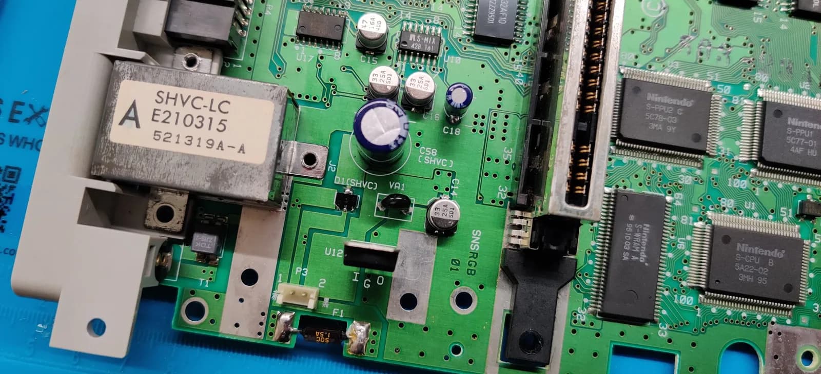 Super Famicom motherboard (green PCB) with electrolytic capacitors and Nintendo ICs, the metal SHVC-LC module (the RF output, with the power jack below and the multiout above), and the D1(SHVC) diode silkscreen-labeled near the centre, the part behind the no-power fault.