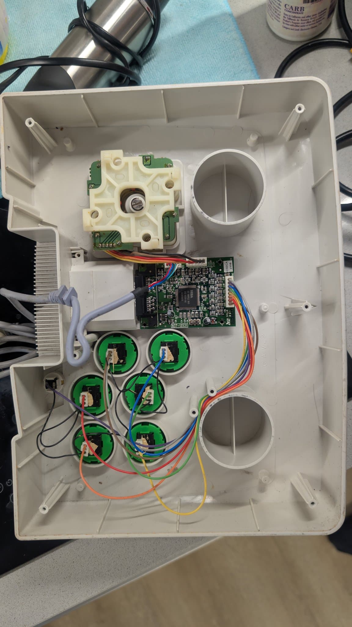Interior of the disassembled Dreamcast arcade stick showing the joystick gate mechanism, the central control PCB with multicolored wiring, six green button switches and the round button ports during refurbishment.