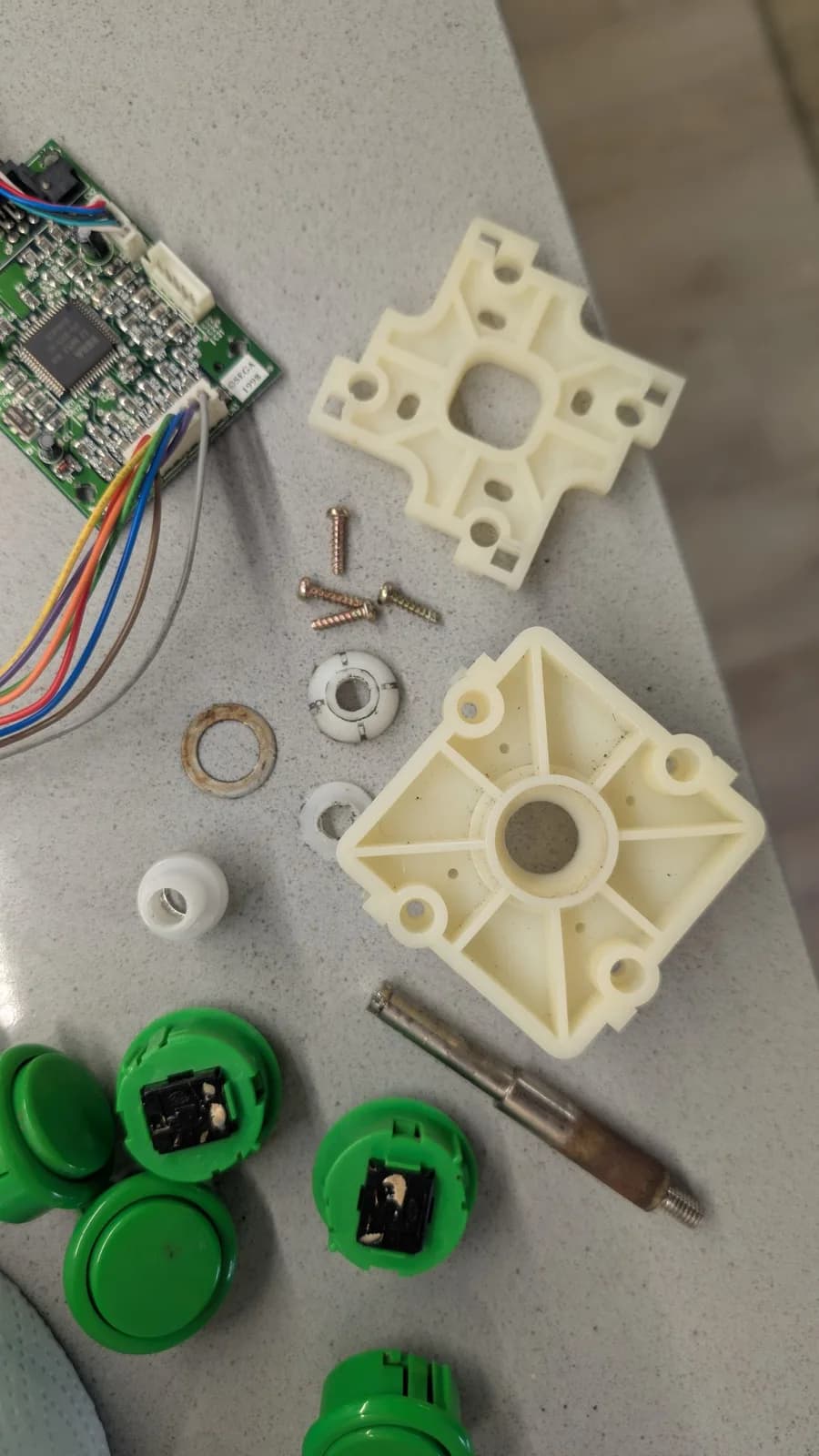 Dreamcast VA0 disassembled components laid out: controller mounting plates, joystick parts, metal screws, circuit board with colored wires, and green button housings undergoing refurbishment.