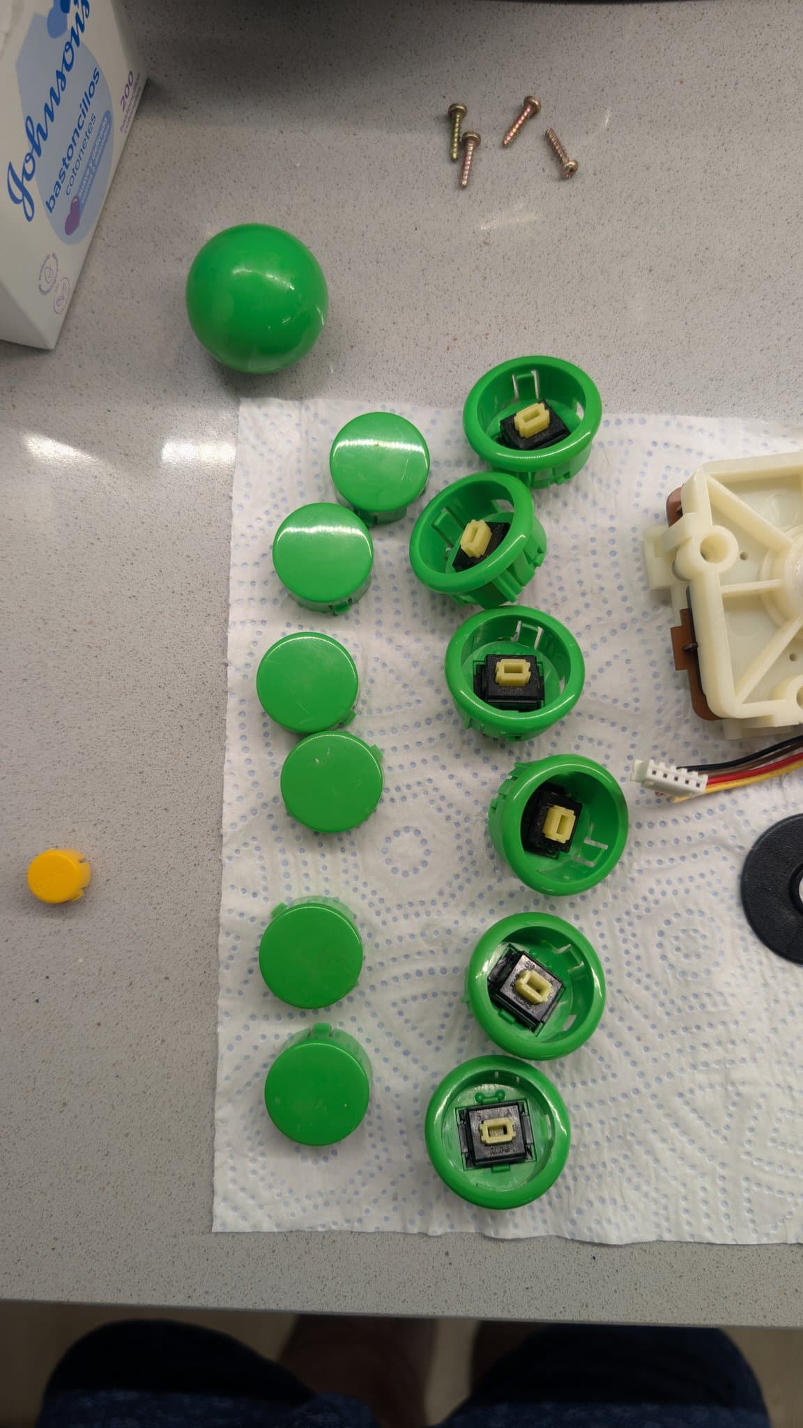 The Dreamcast arcade stick's green buttons opened to their microswitches during cleaning, with brass screws, the green joystick ball and a mounting plate on the paper towel.
