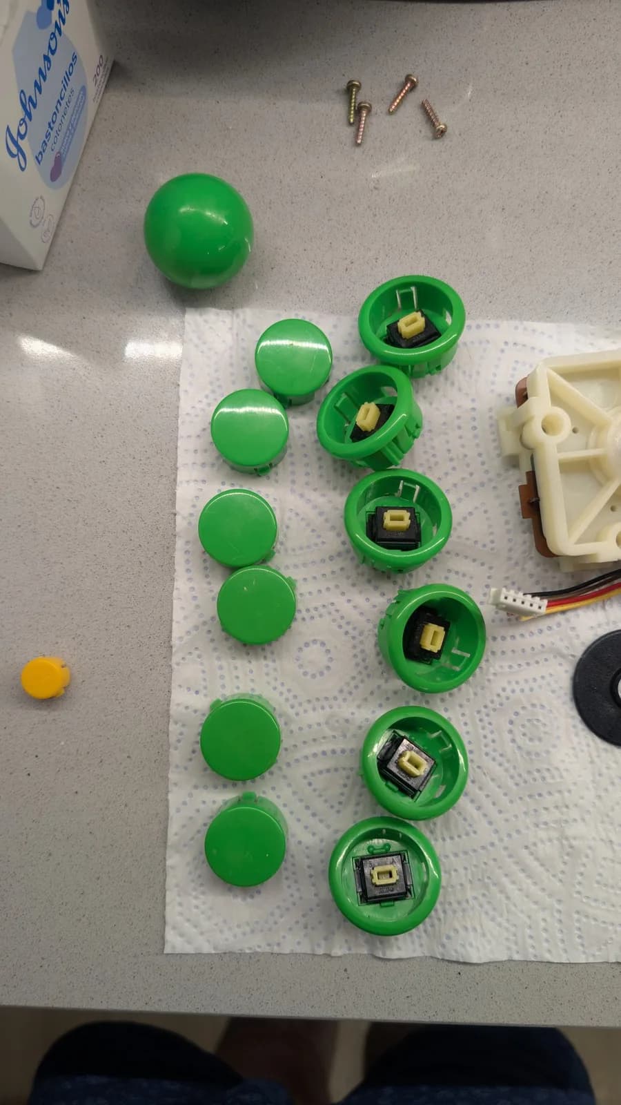 The Dreamcast arcade stick's green buttons opened to their microswitches during cleaning, with brass screws, the green joystick ball and a mounting plate on the paper towel.