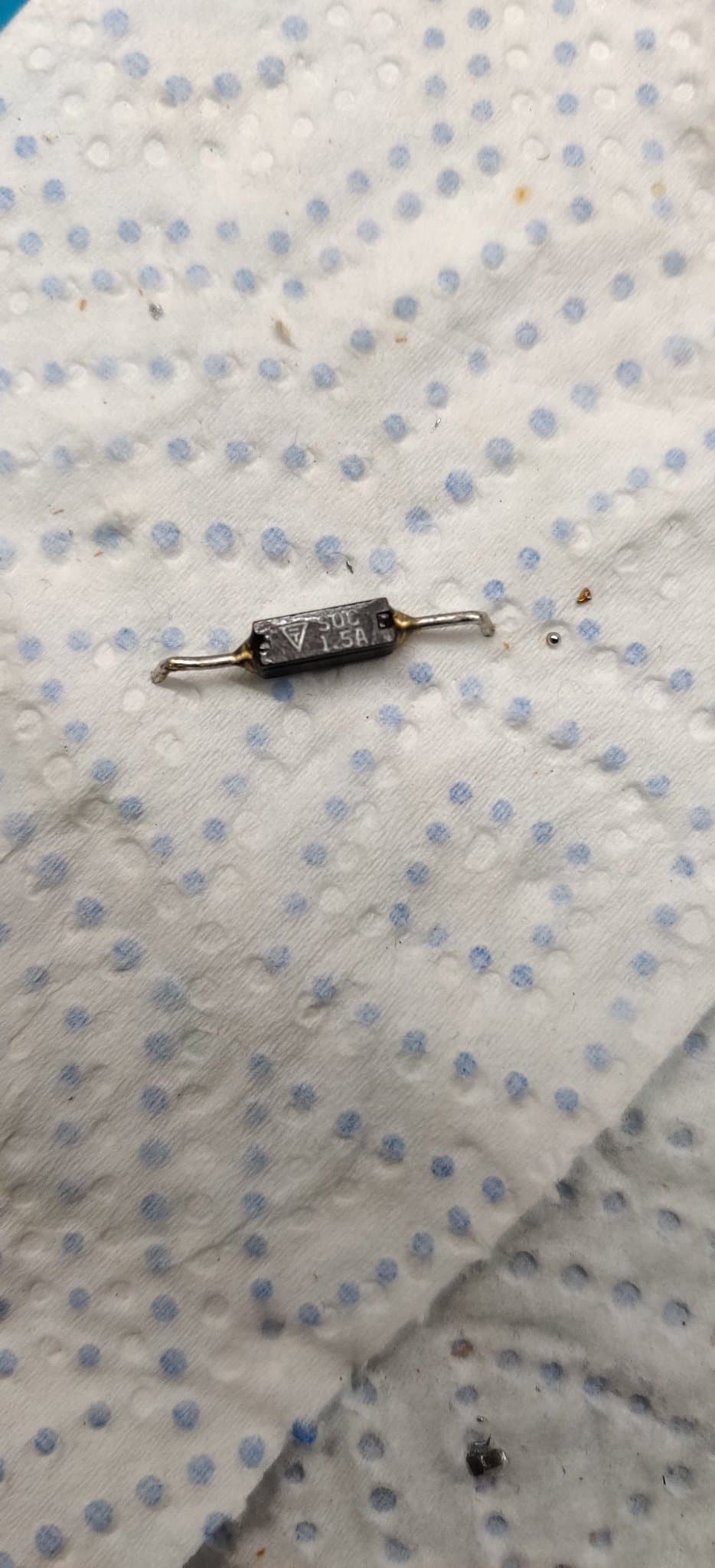 Axial fuse with wire leads on dotted fabric surface, component from Famicom repair with intermittent continuity issue.