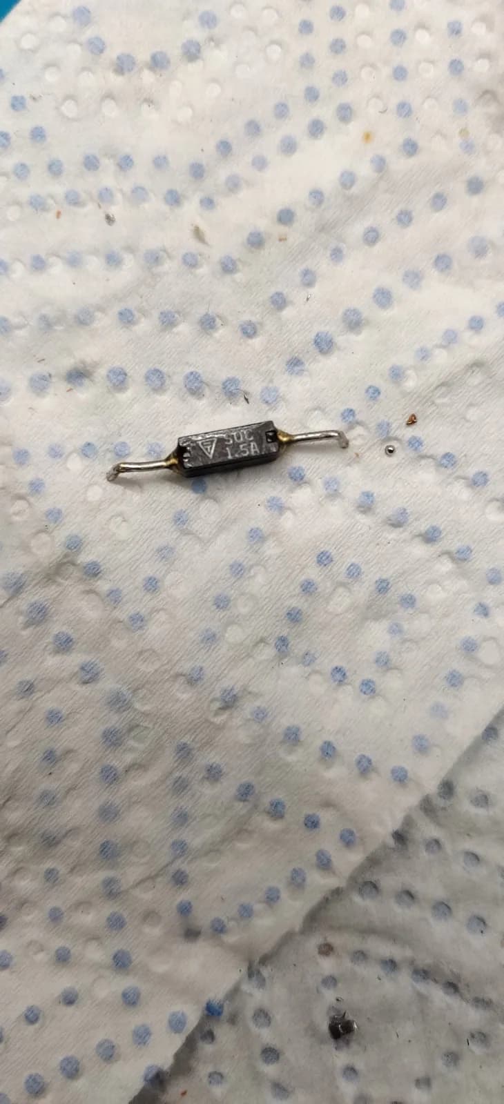 Axial fuse with wire leads on dotted fabric surface, component from Famicom repair with intermittent continuity issue.