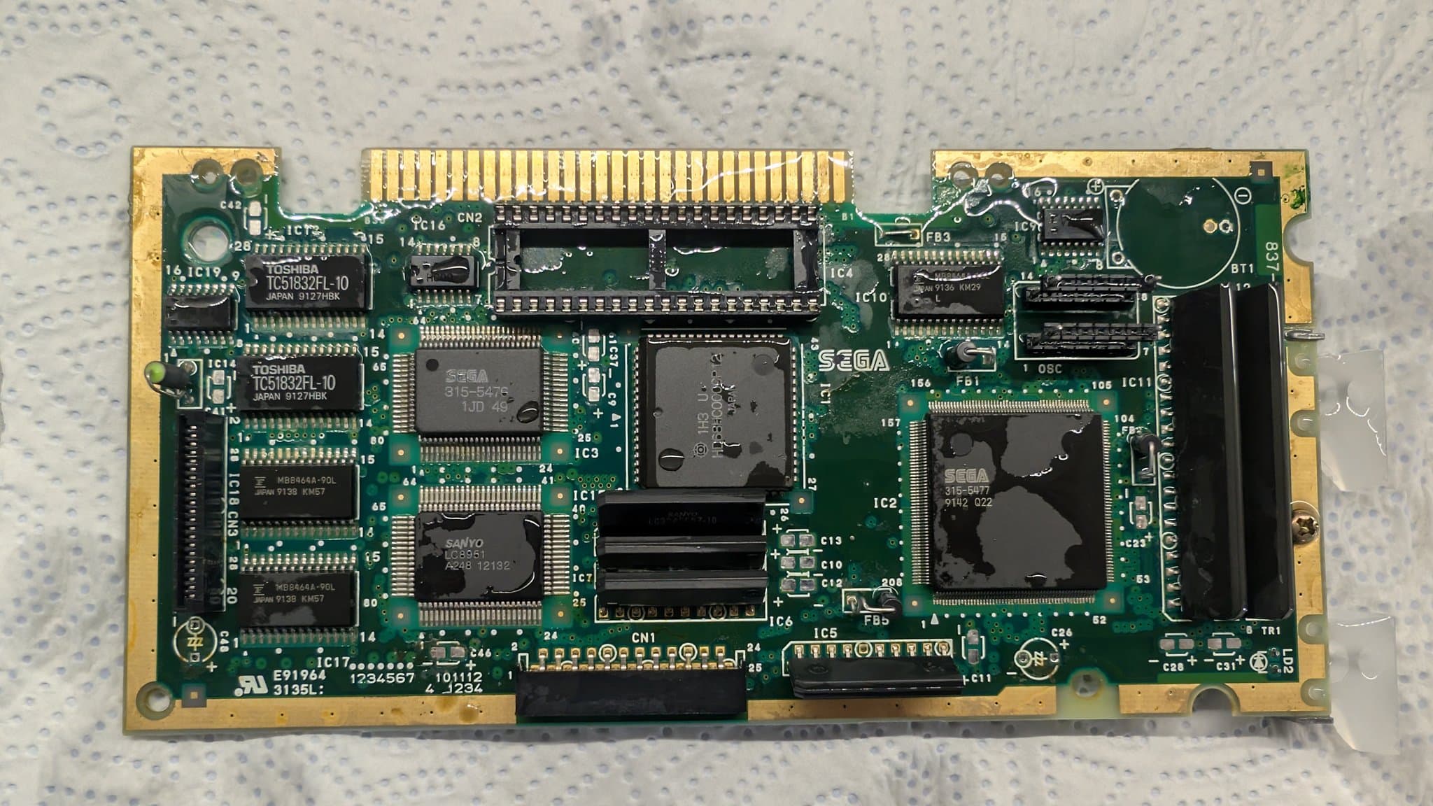 Sega Mega-CD 1 motherboard with multiple leaked capacitors, showing corrosion and damage across the PCB during restoration and recap process.