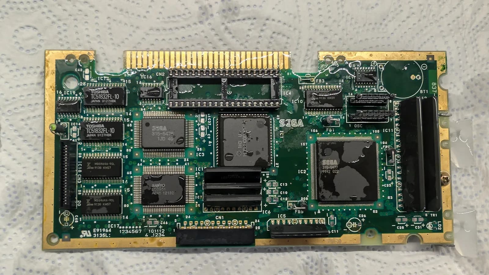 Sega Mega-CD 1 motherboard with multiple leaked capacitors, showing corrosion and damage across the PCB during restoration and recap process.