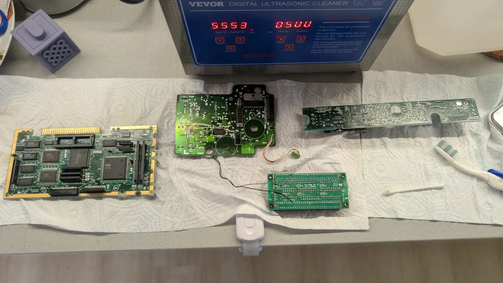 Sega Mega-CD 1 boards after ultrasonic cleaning: main board, drive PCB, and controller board on absorbent paper beneath VEVOR ultrasonic cleaner displaying 5553/9500.