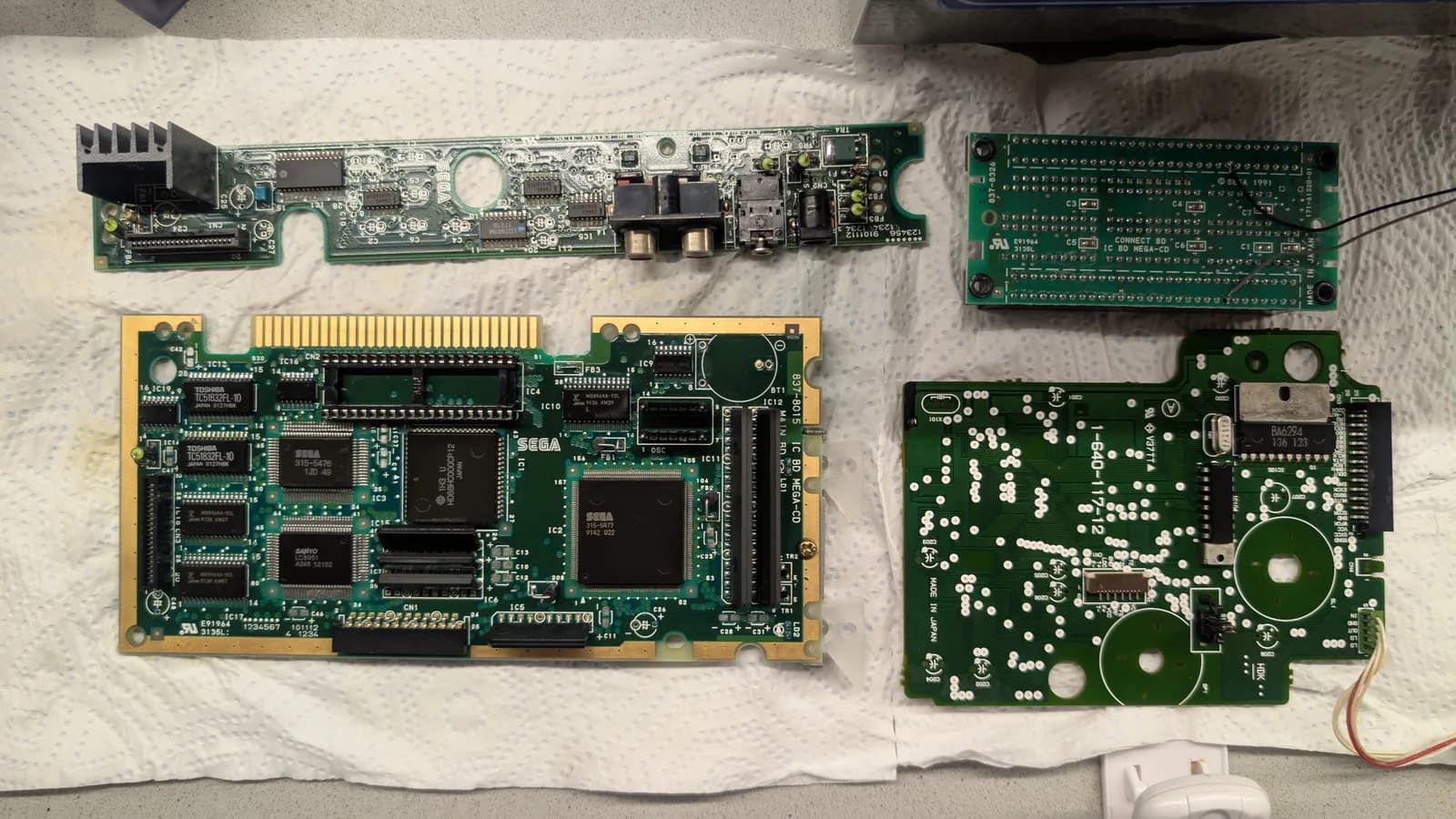 Sega Mega-CD 1 PCBs after ultrasonic cleaning: main board with SEGA chips, PSU board, drive controller, and ribbon cables laid out on white cloth.