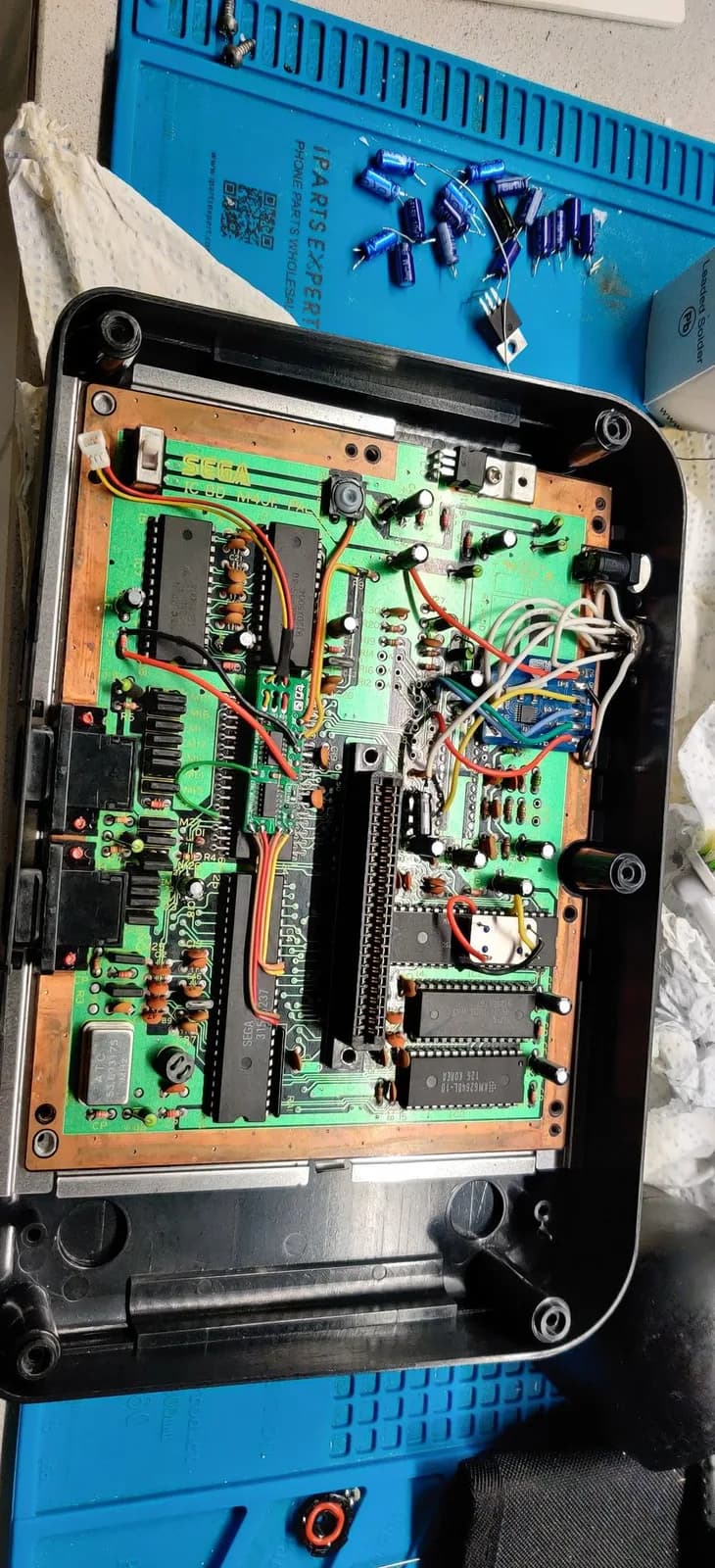 Master System II motherboard with new capacitors installed and voltage regulator replacement in progress; green PCB with IC chips and wiring visible.
