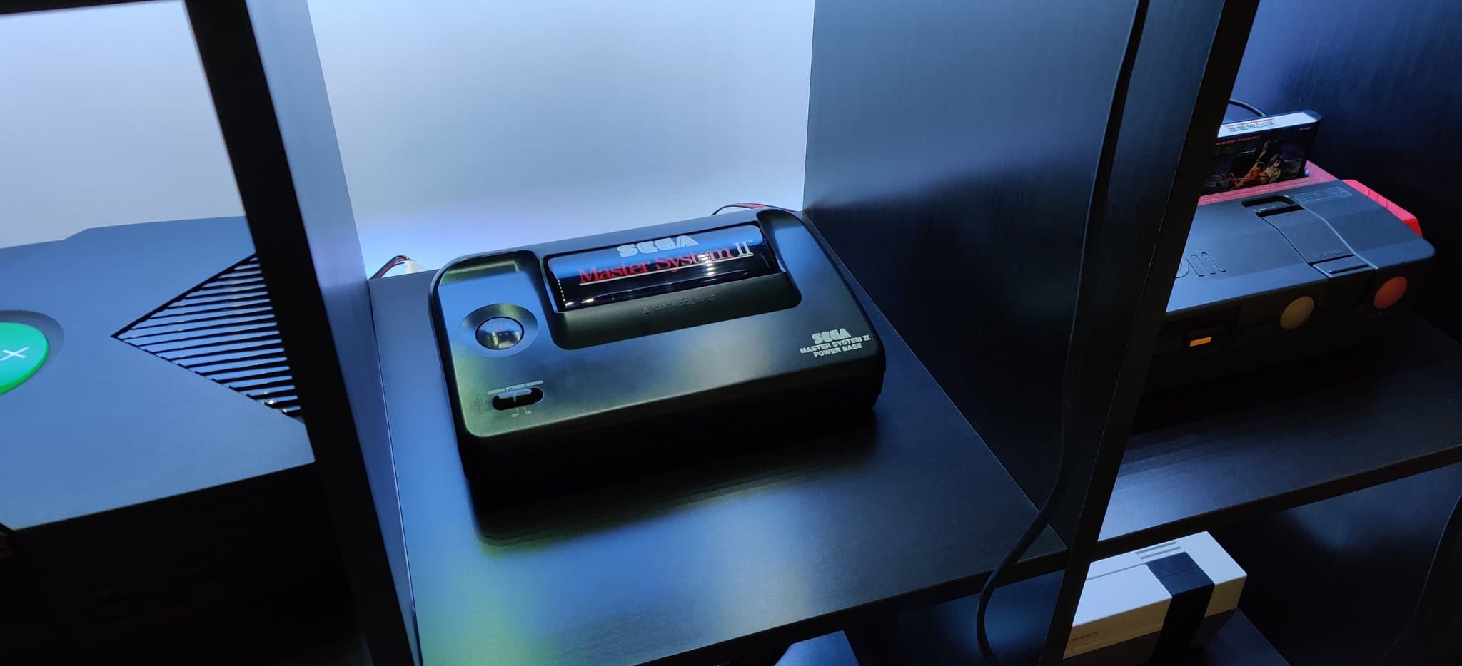 Sega Master System II on display shelf showing RGB mod with new capacitors and voltage regulator installed, ready for testing.