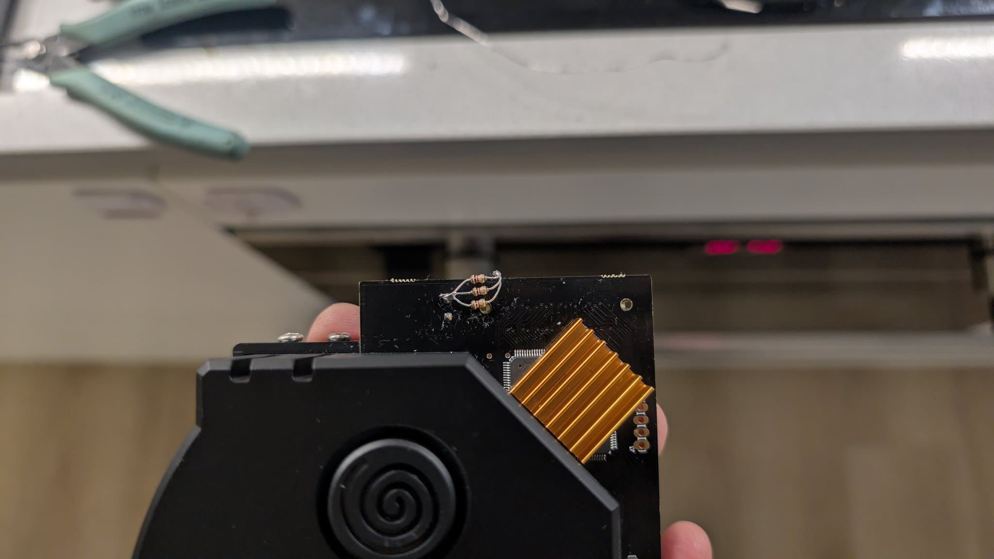 The GDEMU optical-drive emulator, marked with the Dreamcast swirl, held in hand with the hand-built resistor dummy-load soldered to its board and the gold heatsink and flex connector visible.