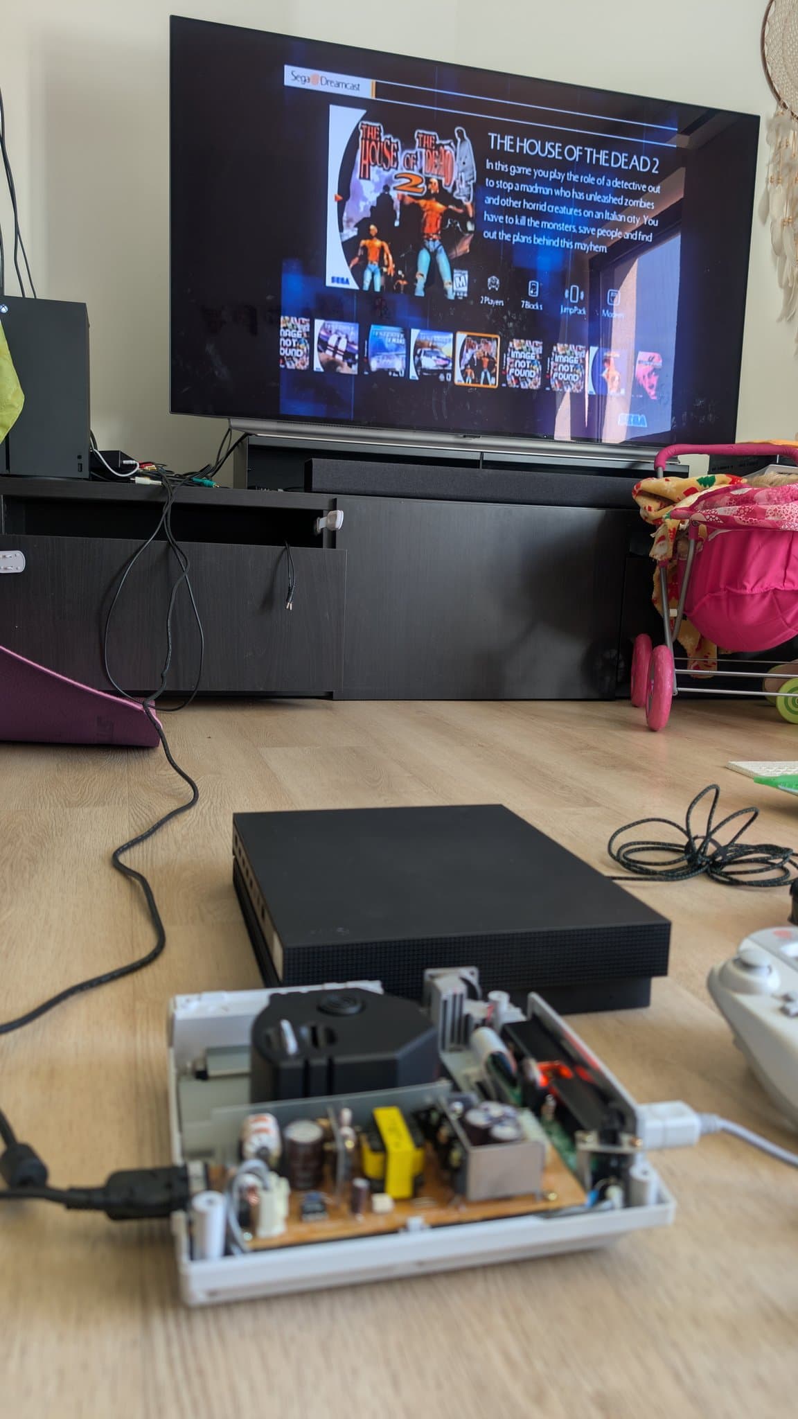 Dreamcast VA0 during burn-in with House of the Dead 2 showing on the TV, the console opened on the floor with its shell off and the internals, including the power supply, exposed.