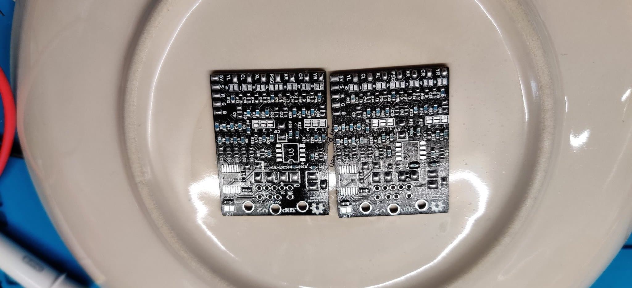 Two assembled 3BP (triple bypass) circuit boards in white dish, showing completed solder joints and components, cleaned with isopropyl alcohol.