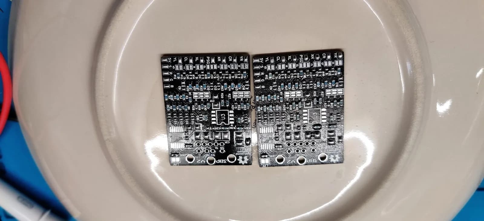The two Triple Bypass (3BP) V2 boards in a beige dish after hot-air reflow and an isopropyl clean, the SMD components pulled neatly into place by the surface tension of the molten solder (ICs not fitted yet).