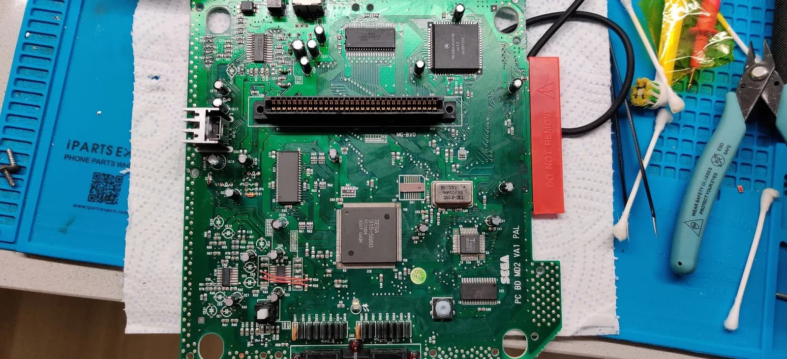 Sega Mega Drive II VA1 mainboard (silkscreen "PC BD MD2 VA1 PAL") part-way through the Triple Bypass install: the capacitors the 3BP requires removing are off the board (alongside newer caps from earlier work), R72 and R73 removed with their pads bridged by solder, and R22 and R24 also removed, the signal from each one's right pad routed by wire to the left pad of the removed R33 and R36 respectively.