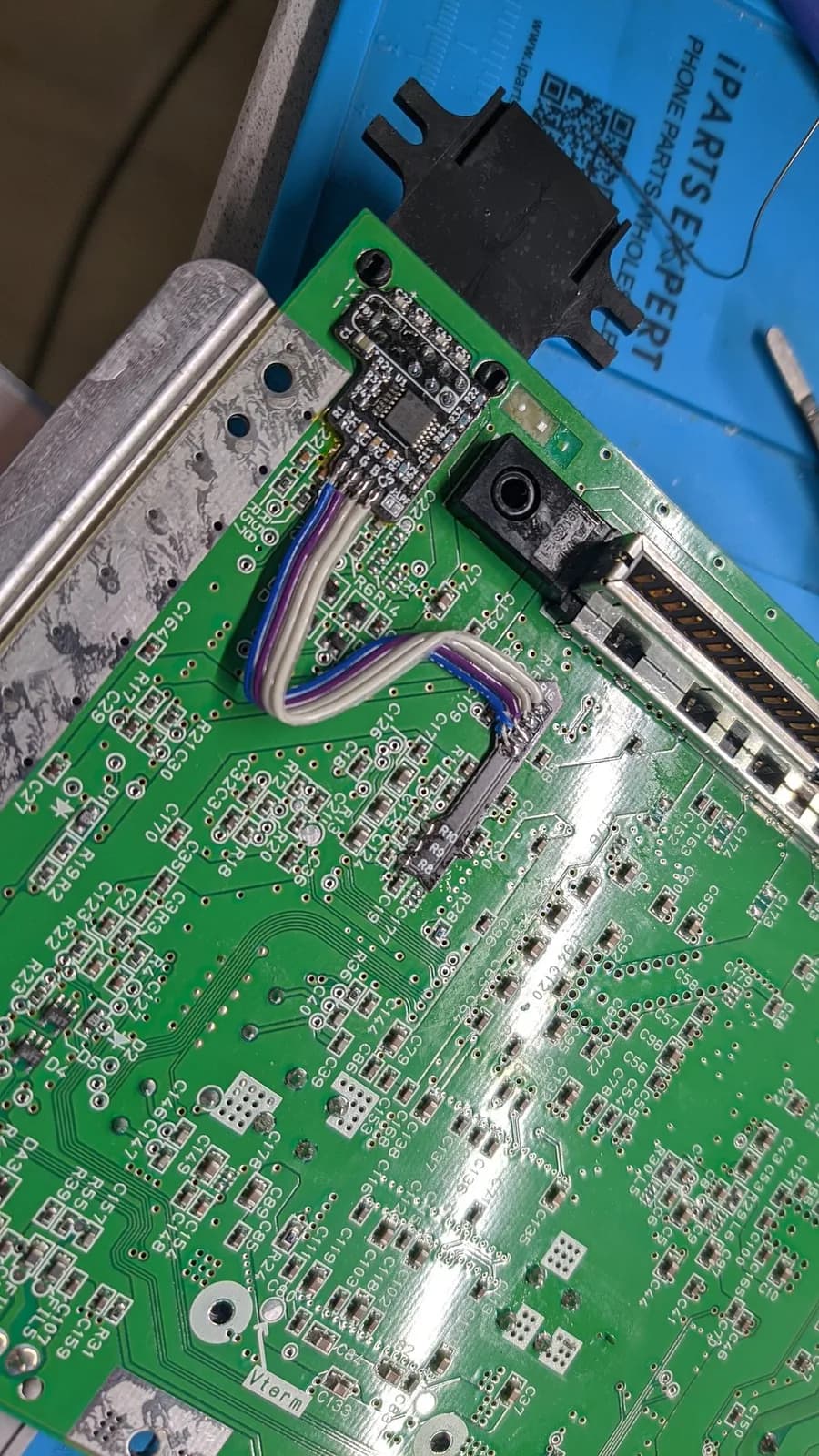 Close-up of the installed N64 RGB mod: the green N64 motherboard seen from its underside, with the RGB amp soldered onto the multi-out port, a wiring harness, and the black connector mounted on the metal shielding.