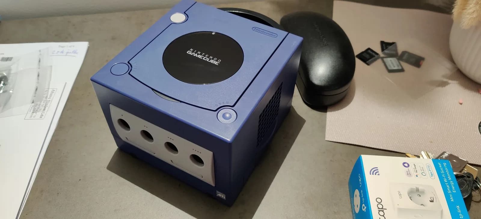Indigo GameCube on a desk beside a prescription-glasses case, with documentation and SD cards nearby, after the retrobrite.