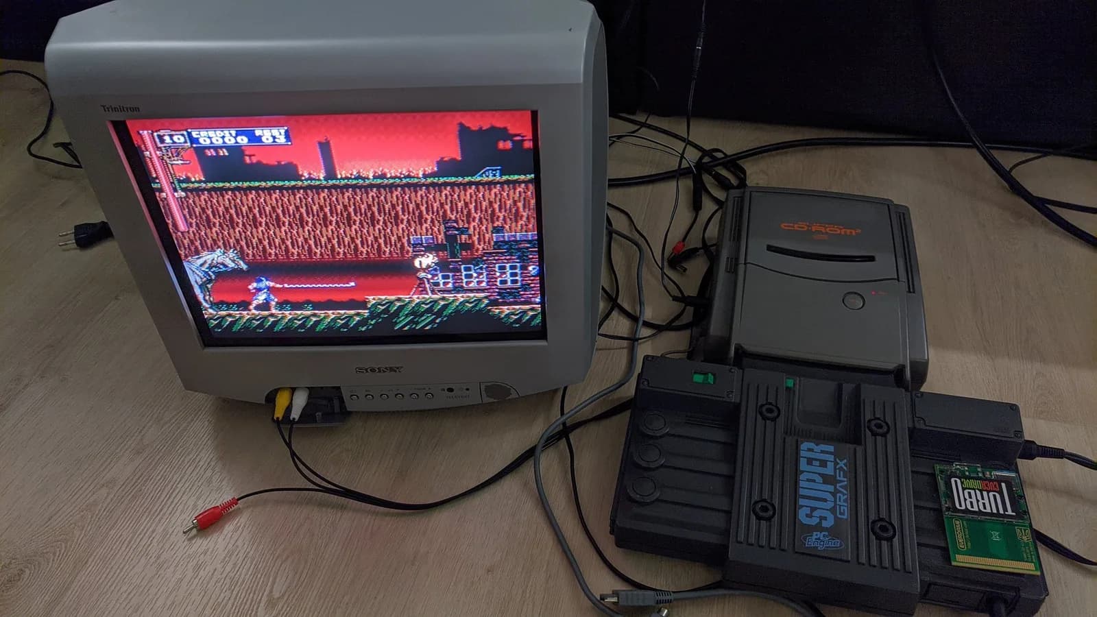 A grey PC Engine SuperGrafx with the Super CD-ROM2 docked on top, connected to a Sony Trinitron CRT running Castlevania: Rondo of Blood after the refurbishment, the disc drive reading and video output working again. A green Turbo EverDrive flashcart rests on the shell to the right.