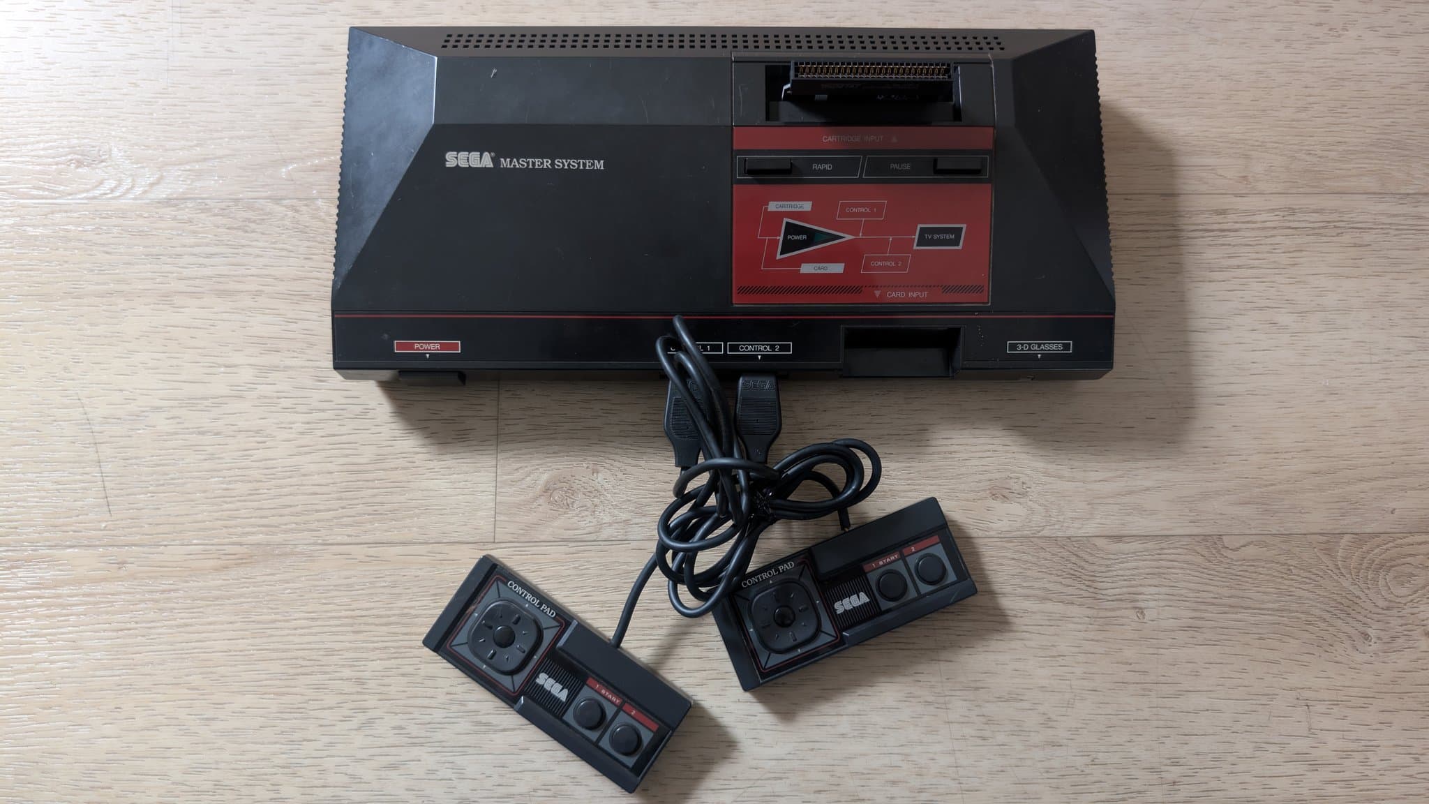 Sega Master System MK-2000 with two controllers connected via cable, displayed on wooden surface during refurbishment.