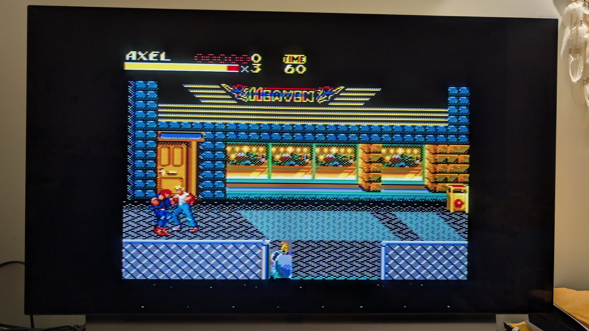 Master System displaying Streets of Rage II gameplay: the character Axel fights an enemy on a city street outside a storefront, with the AXEL name, a health bar, a lives counter and a TIME value across the top of the screen.
