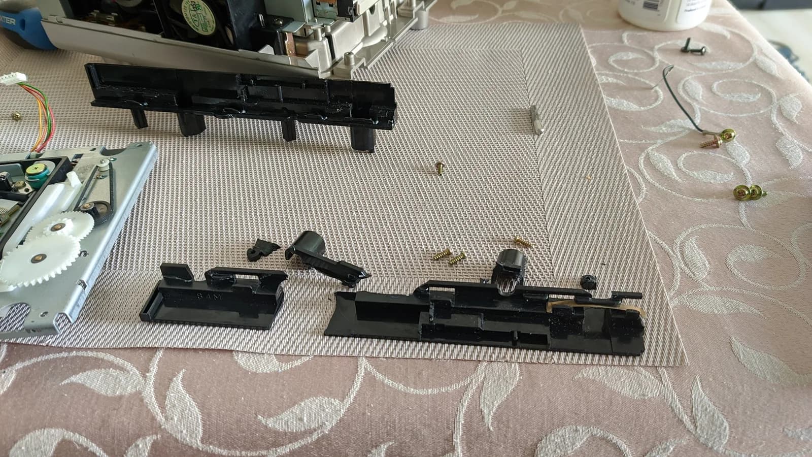 Disassembled Panasonic Q optical drive rails laid out for comparison; one 3D printed replacement rail next to original shattered rail pieces.