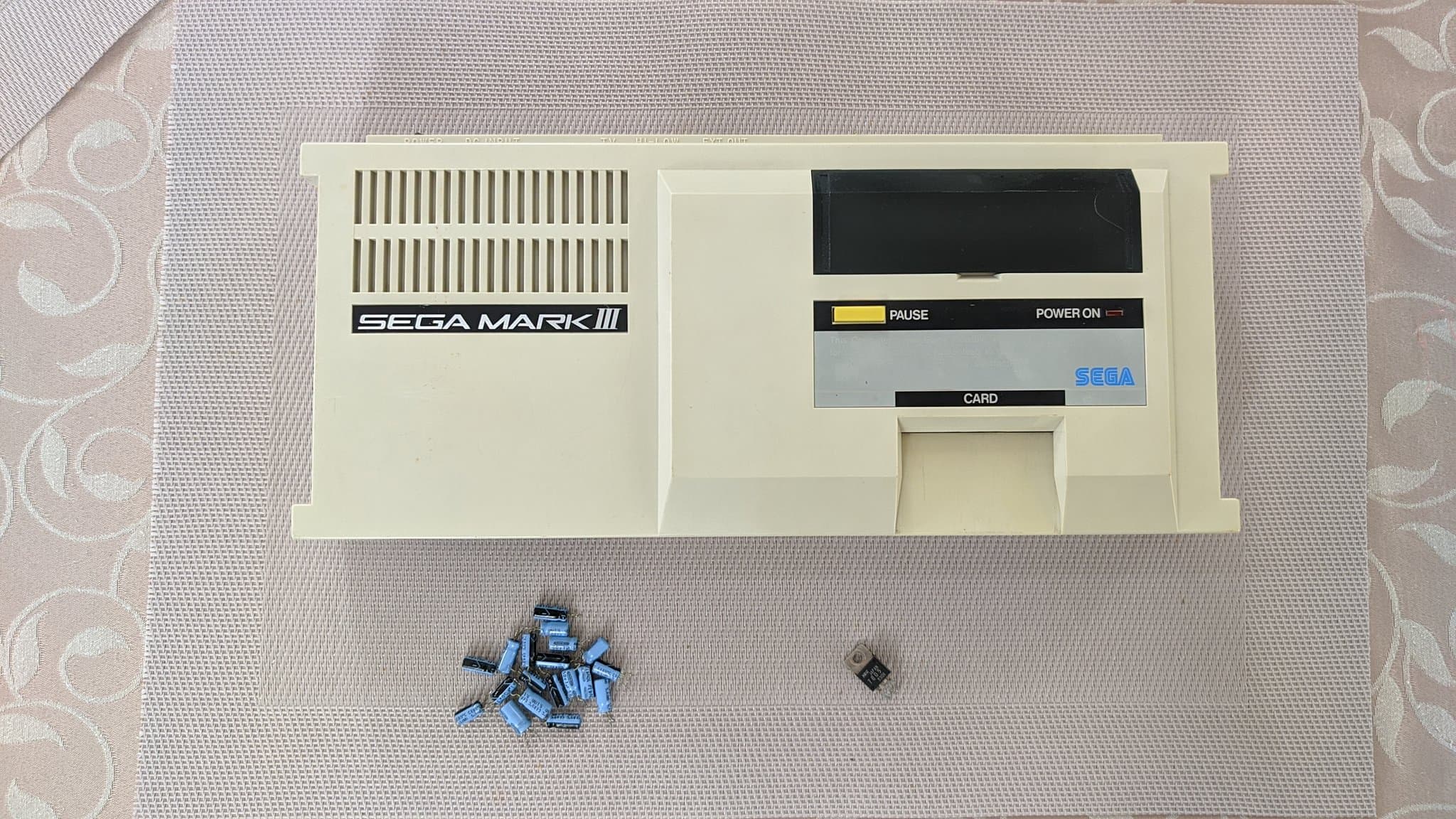 Sega Mark III with removed capacitors and voltage regulator displayed below the console during refurbishment and retrobrighting restoration.